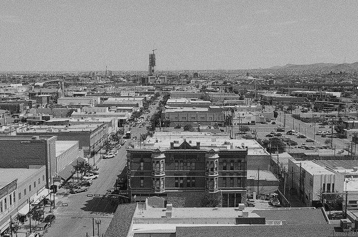 An elevated view shows a city with many buildings and streets with cars, with mountains in the distance.