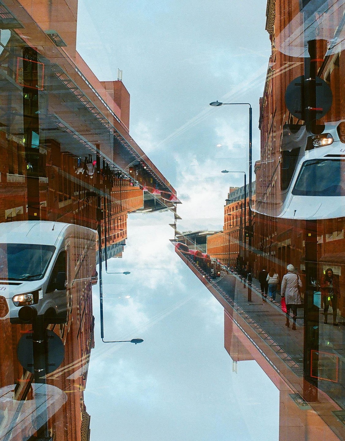 A double exposure shows a street with buildings, people, and a van reflected in a window.