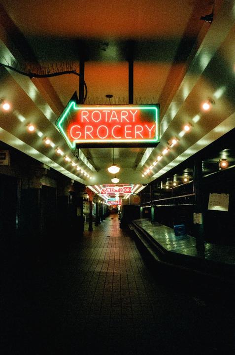 A neon sign for "Rotary Grocery" points down a long, empty hallway lined with lights.