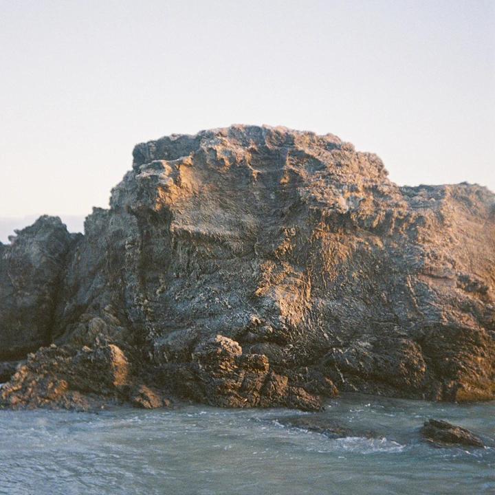A large rock formation is partially submerged in water under a bright sky.