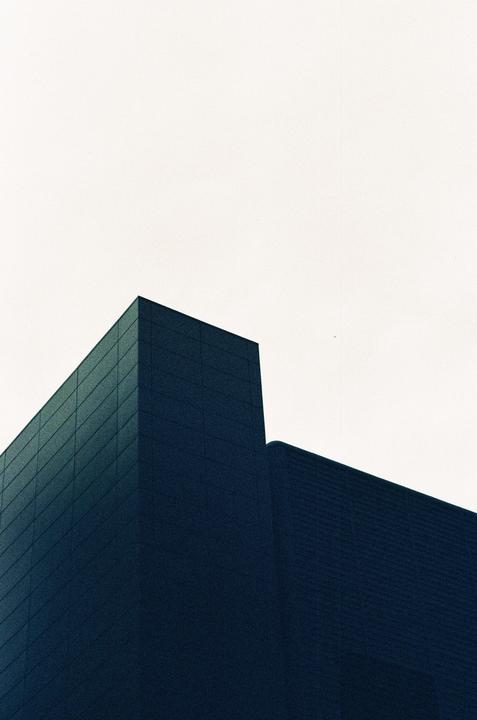 Two dark buildings with textured facades are shown against a bright, overcast sky.