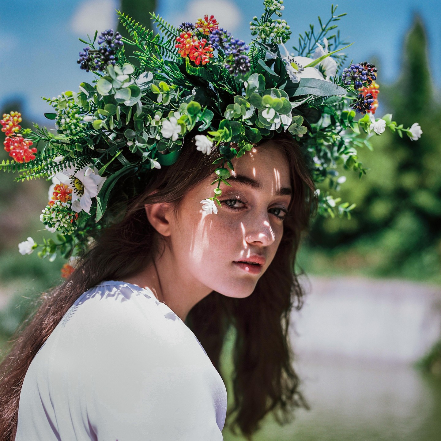 A woman wearing a flower crown looks over her shoulder at the viewer.
