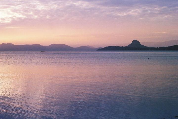 A body of water is surrounded by mountains under a colorful sky.