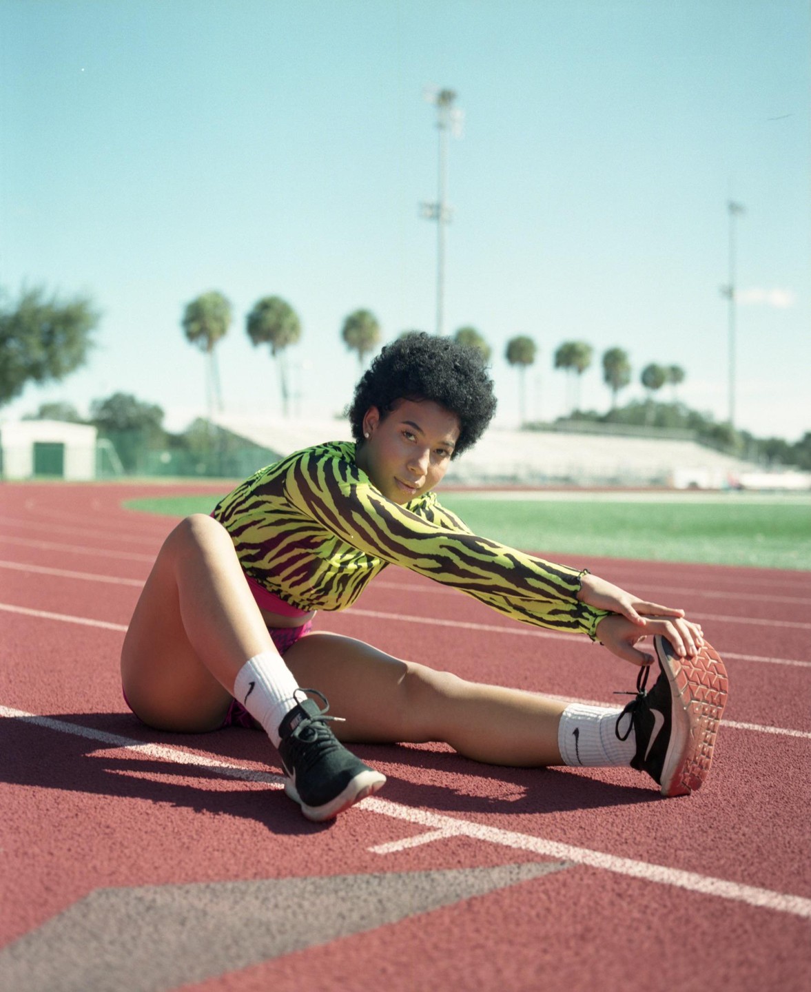 A woman in a neon zebra print top stretches on a running track.