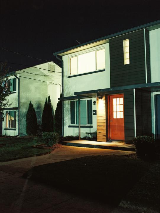 A house with a bright orange door and illuminated windows stands at night.