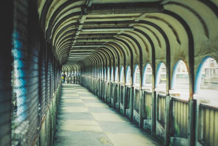 A person walks down a long, arched pedestrian bridge with a checkered floor.