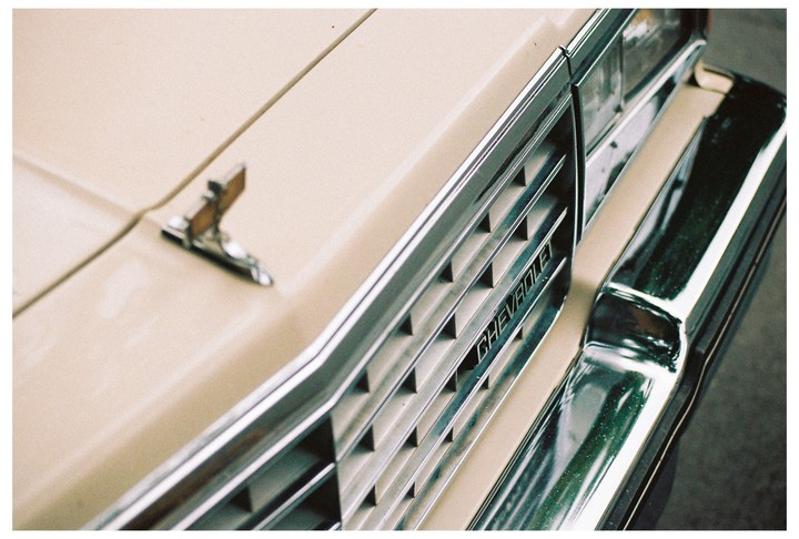 A close-up shot shows the front grille and hood ornament of a beige Chevrolet car.