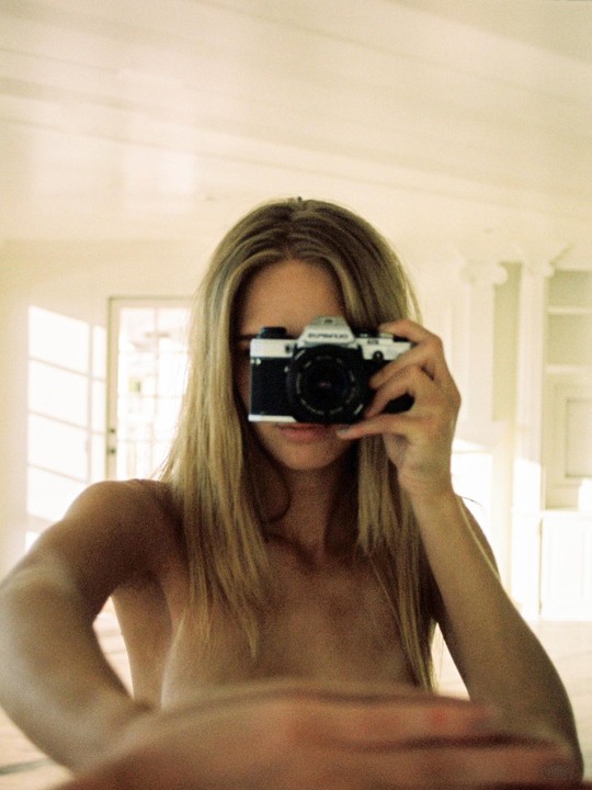 A woman with long hair takes a mirror self-portrait with a camera covering her face.