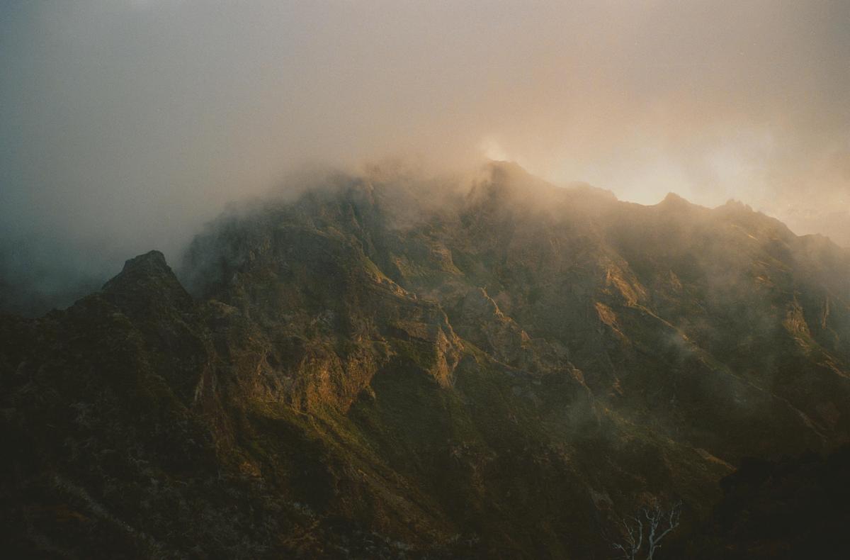 A mountain range is covered in fog with a golden glow from the sun.