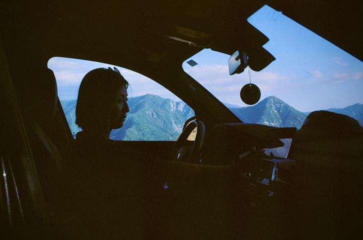 A woman sits in a car looking out at a mountain landscape.