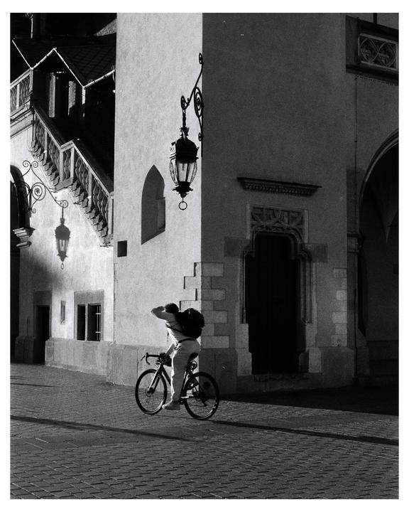A man on a bicycle is riding past a building with ornate lanterns and a staircase.