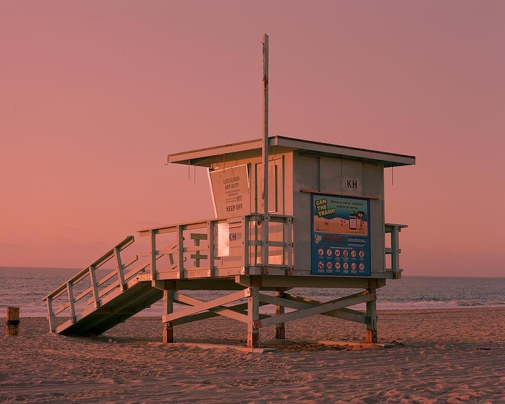 A lifeguard tower stands on a sandy beach with the ocean in the background under a pink sky.