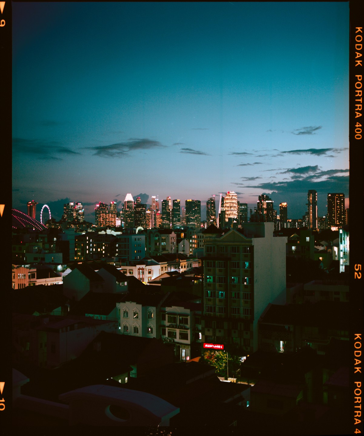 A city skyline with illuminated buildings is visible at dusk, with a ferris wheel on the left.
