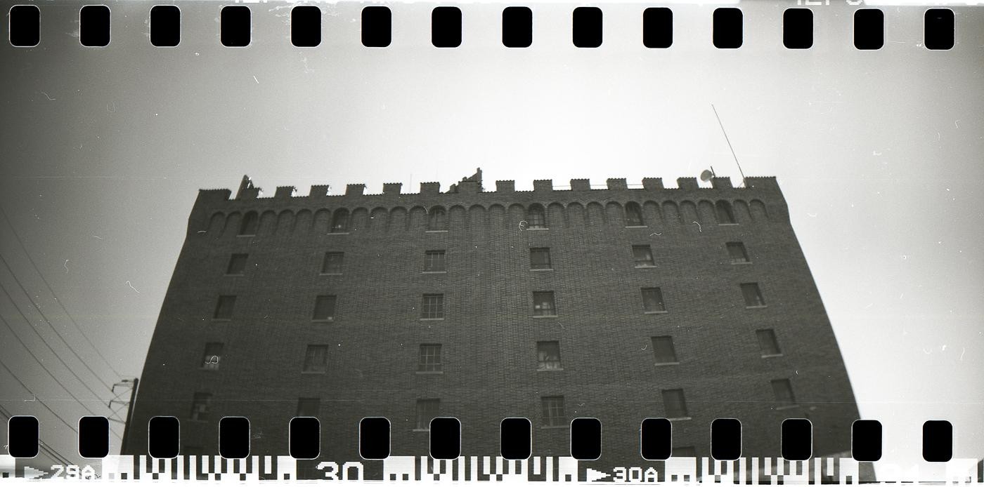 A low-angle view shows a brick building with a crenellated roofline against a bright sky.