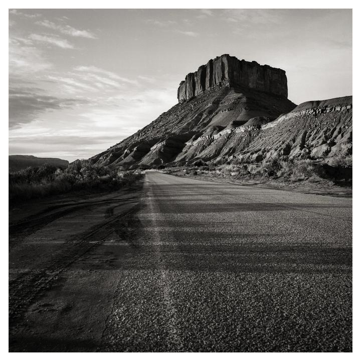 A road leads towards a large mesa under a cloudy sky.