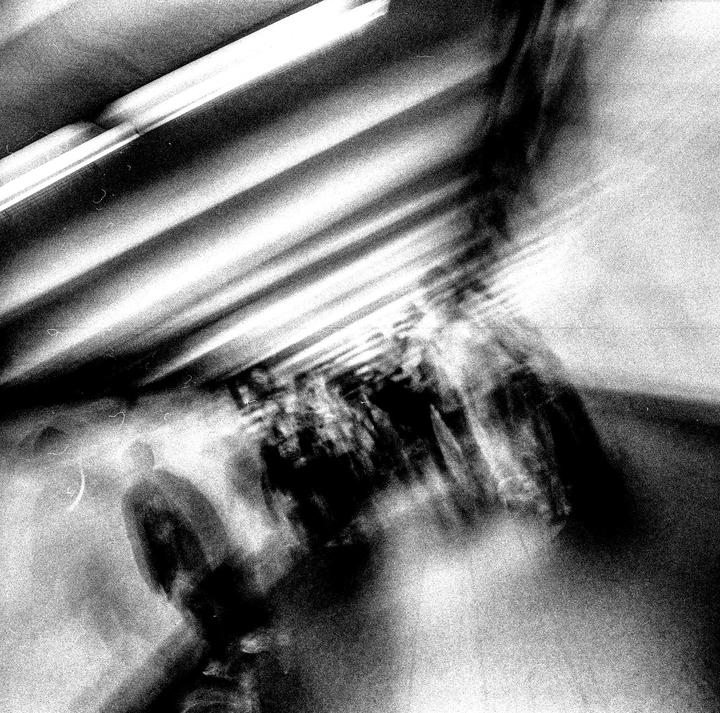 A blurry black and white image shows people walking in a tunnel with bright lights on the ceiling.