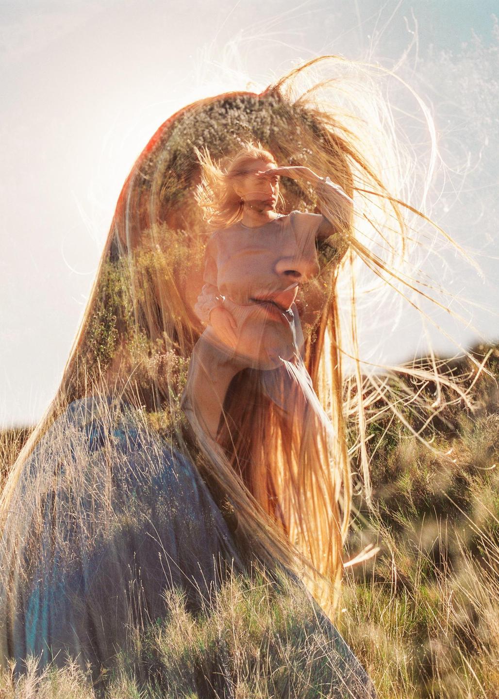 A double exposure shows a woman with long hair in a field of tall grass, with a second exposure of a woman shielding her eyes from the sun superimposed over her face.