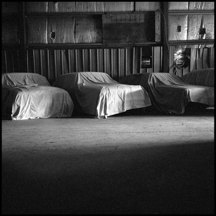 Three cars covered with sheets are parked in a dark garage.