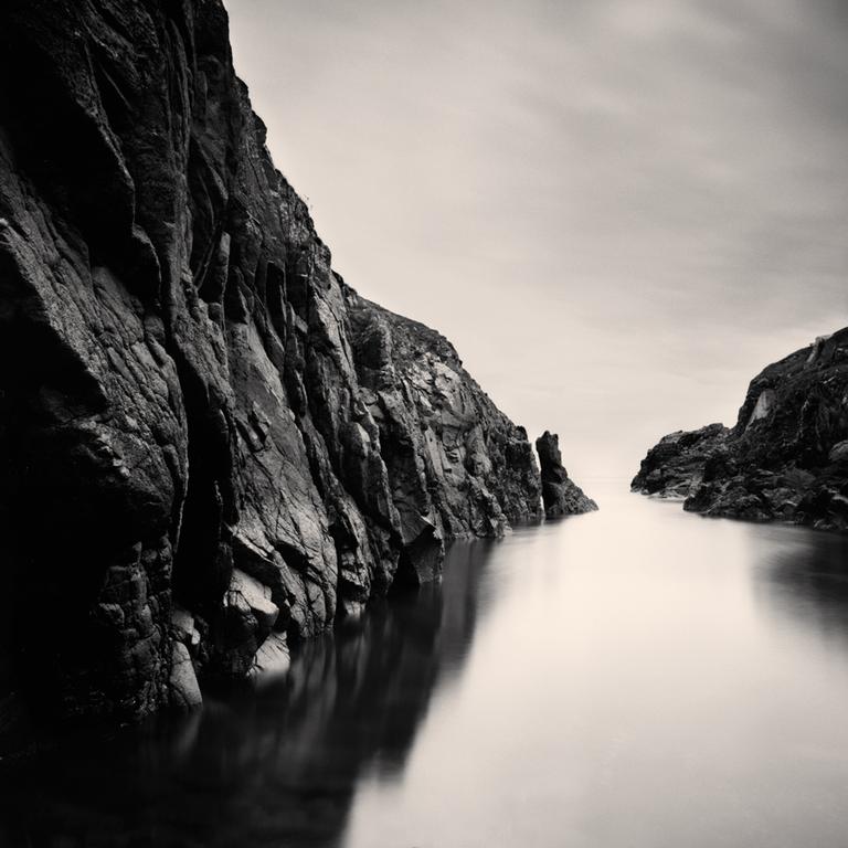 A body of water is surrounded by tall, rocky cliffs under a bright sky.