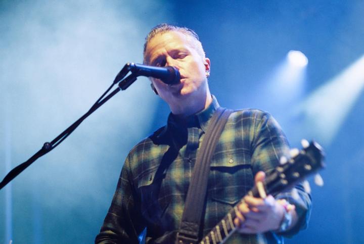 A man sings into a microphone while playing a guitar on a stage.