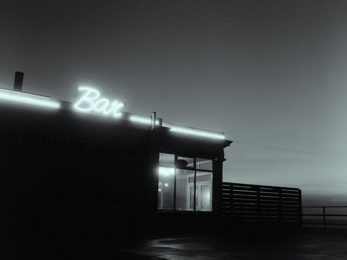 A neon sign spelling "Bar" illuminates the facade of a building at night.