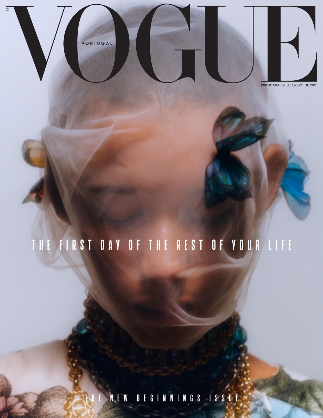 A woman's face is covered by a sheer veil with butterflies on it, and she wears a gold and blue necklace.