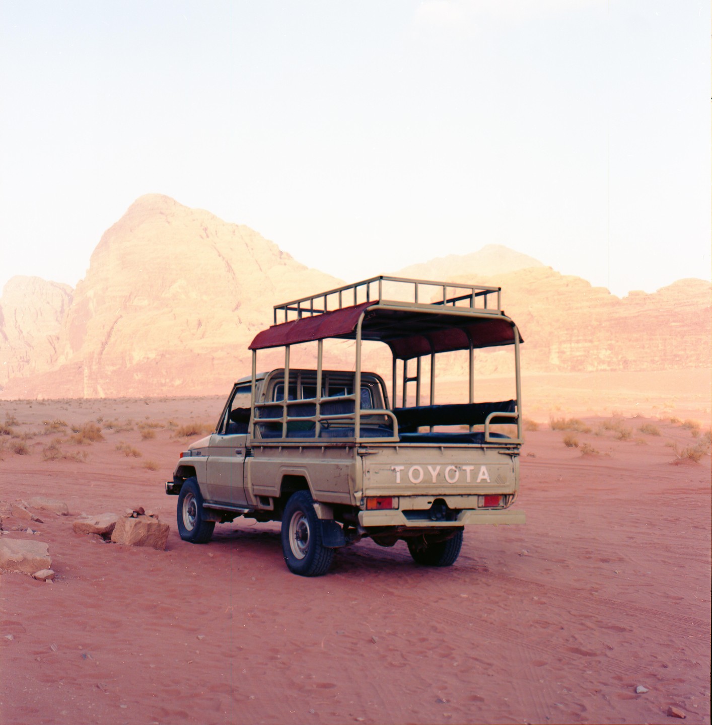A beige Toyota pickup truck with a canopy is parked in a desert landscape with mountains in the background.