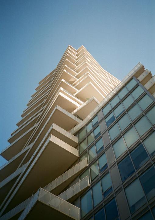 A tall building with many balconies and windows rises into a clear sky.