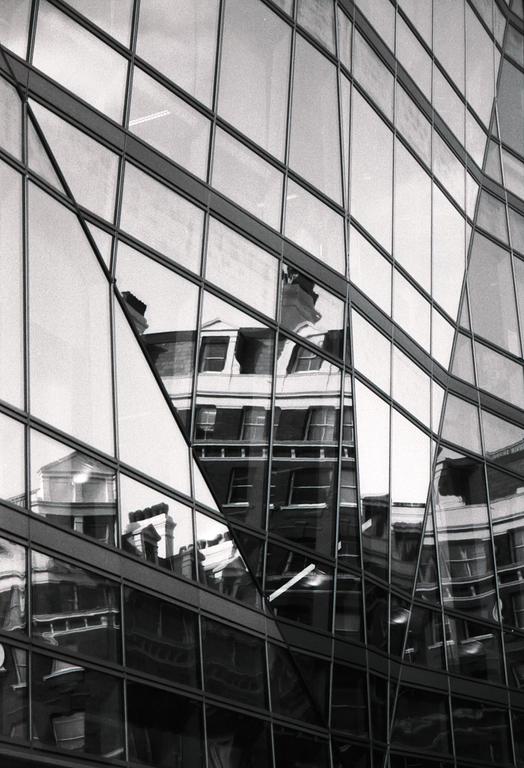 An old building is reflected in the glass facade of a modern building.
