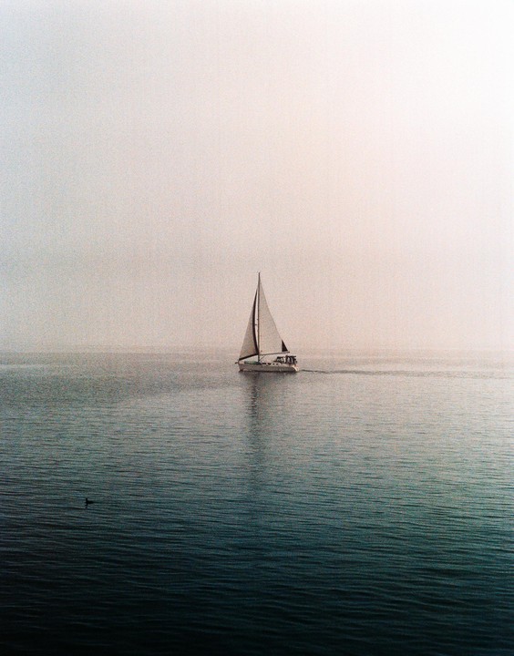 A sailboat moves across the water on a foggy day.