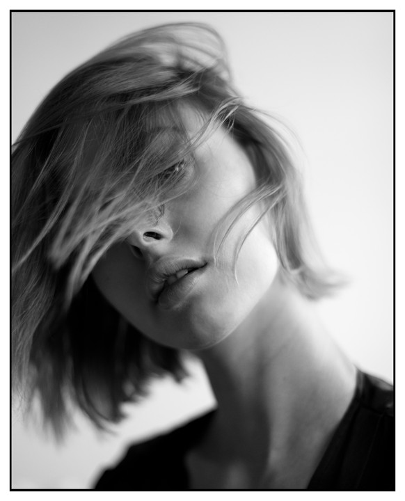 A woman with short hair looks at the camera with her head tilted.