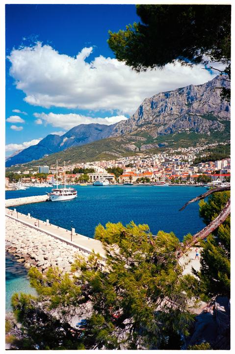 A scenic view of a coastal town with a harbor, mountains, and a clear blue sky.