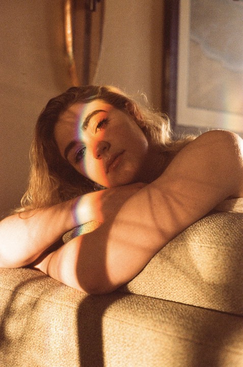 A woman rests her head on a couch with a rainbow light reflection across her face and arm.