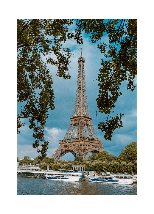 The Eiffel Tower is visible through tree branches, with boats docked on the river below.