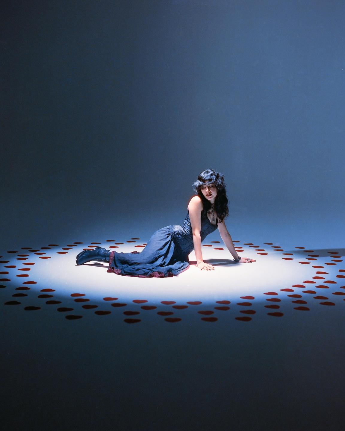 A woman in a blue dress is sitting on the floor surrounded by red heart shapes.