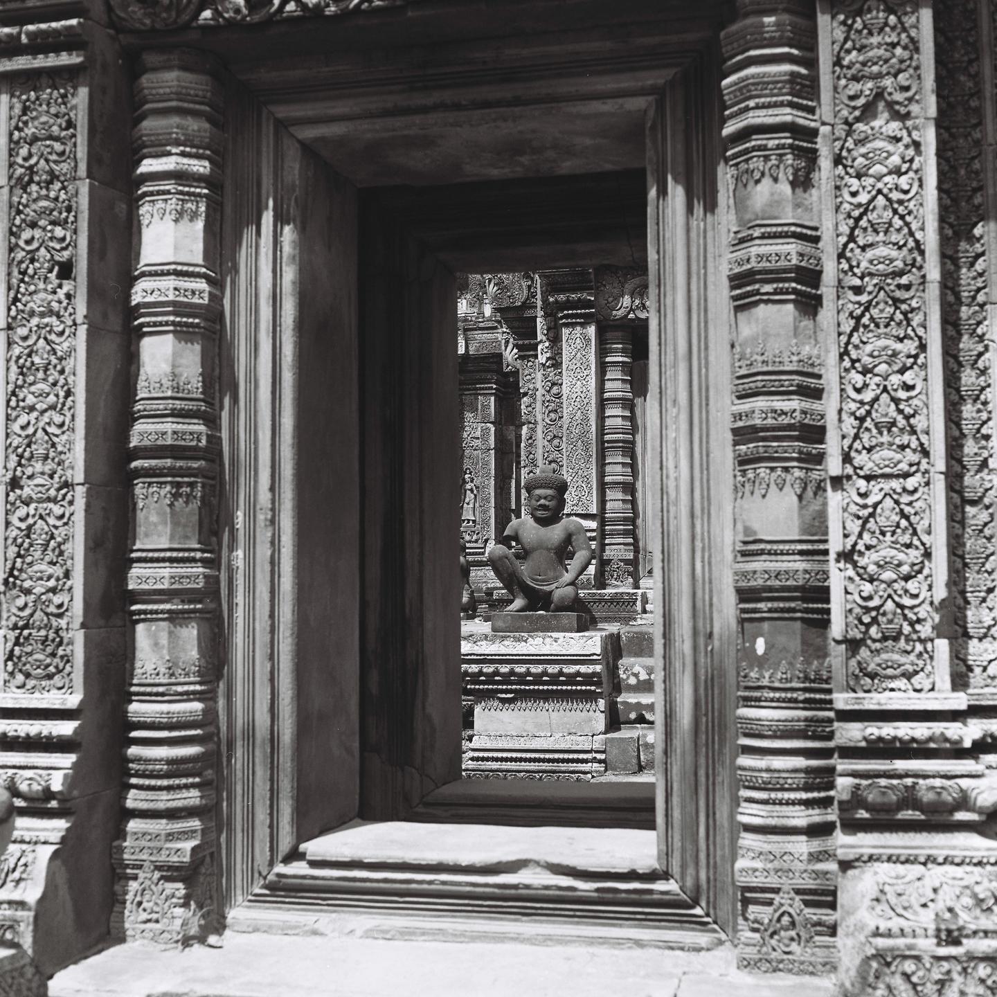 A stone statue of a squatting figure is visible through an ornate doorway.