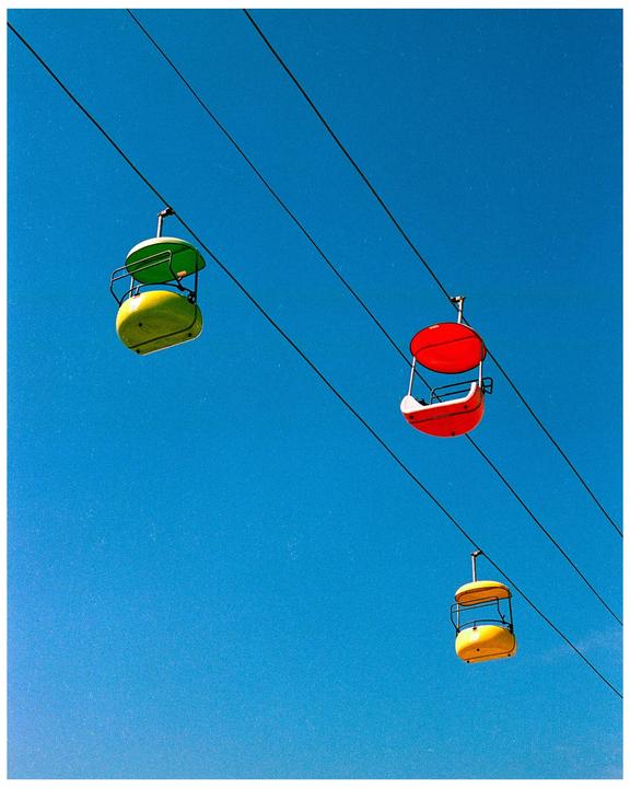 Three colorful gondolas are suspended by cables against a clear blue sky.