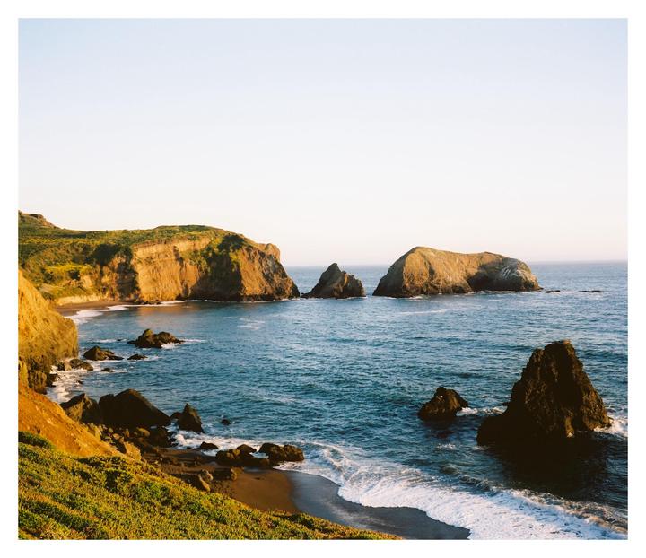 A rocky coastline with cliffs and sea stacks is illuminated by the golden hour sun.