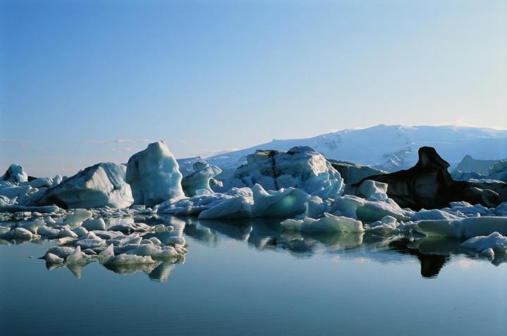 Icebergs float on a body of water with snow-covered mountains in the background.