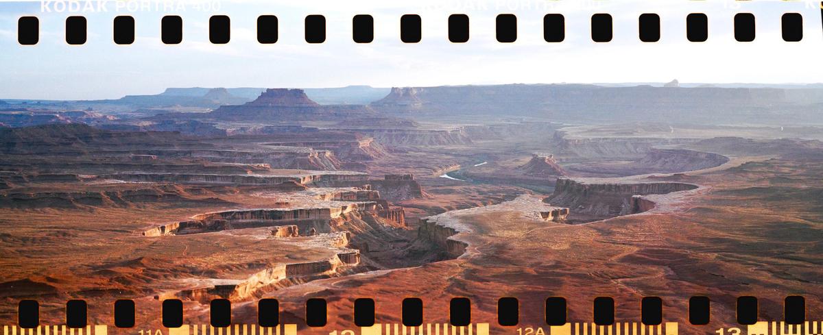 A vast canyon landscape with a winding river is visible under a hazy sky.