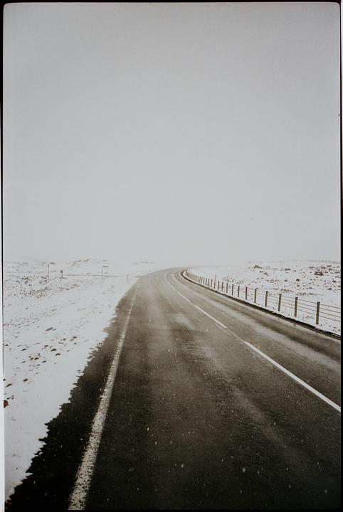A road curves through a snowy landscape under a white sky.