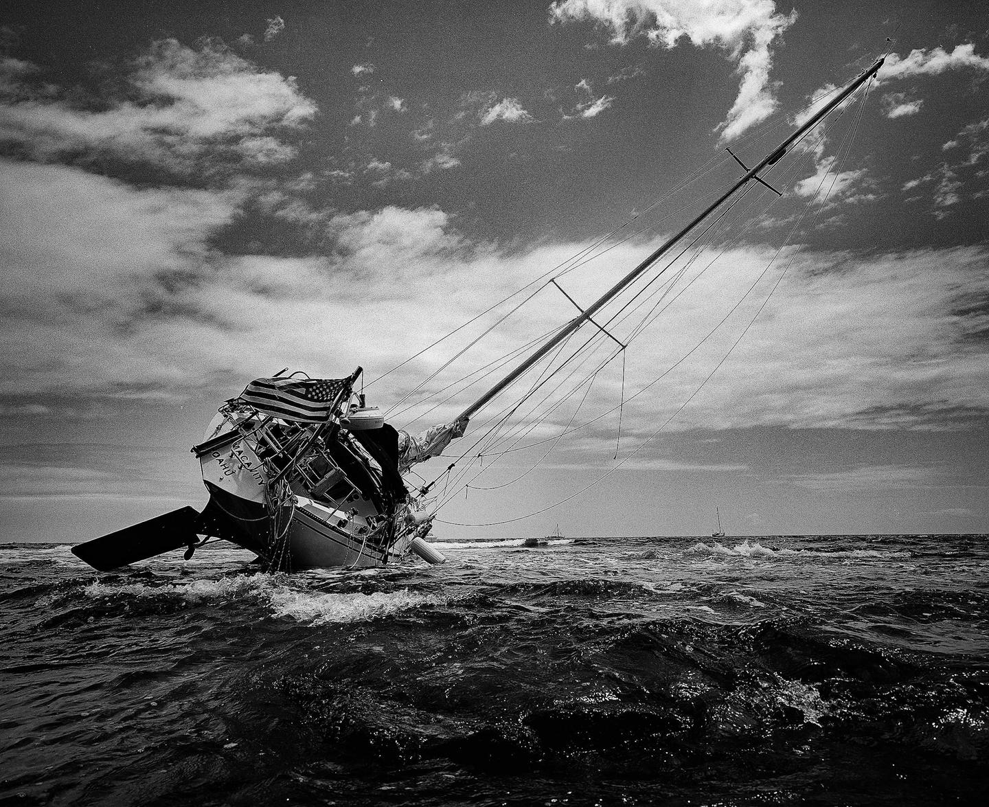 A sailboat with an American flag is grounded in rough water under a cloudy sky.