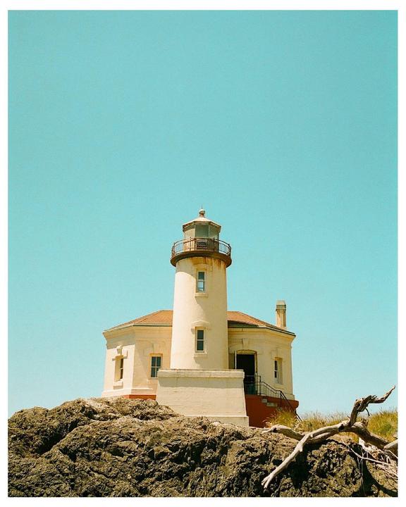 A lighthouse stands on a rocky cliff under a clear blue sky.