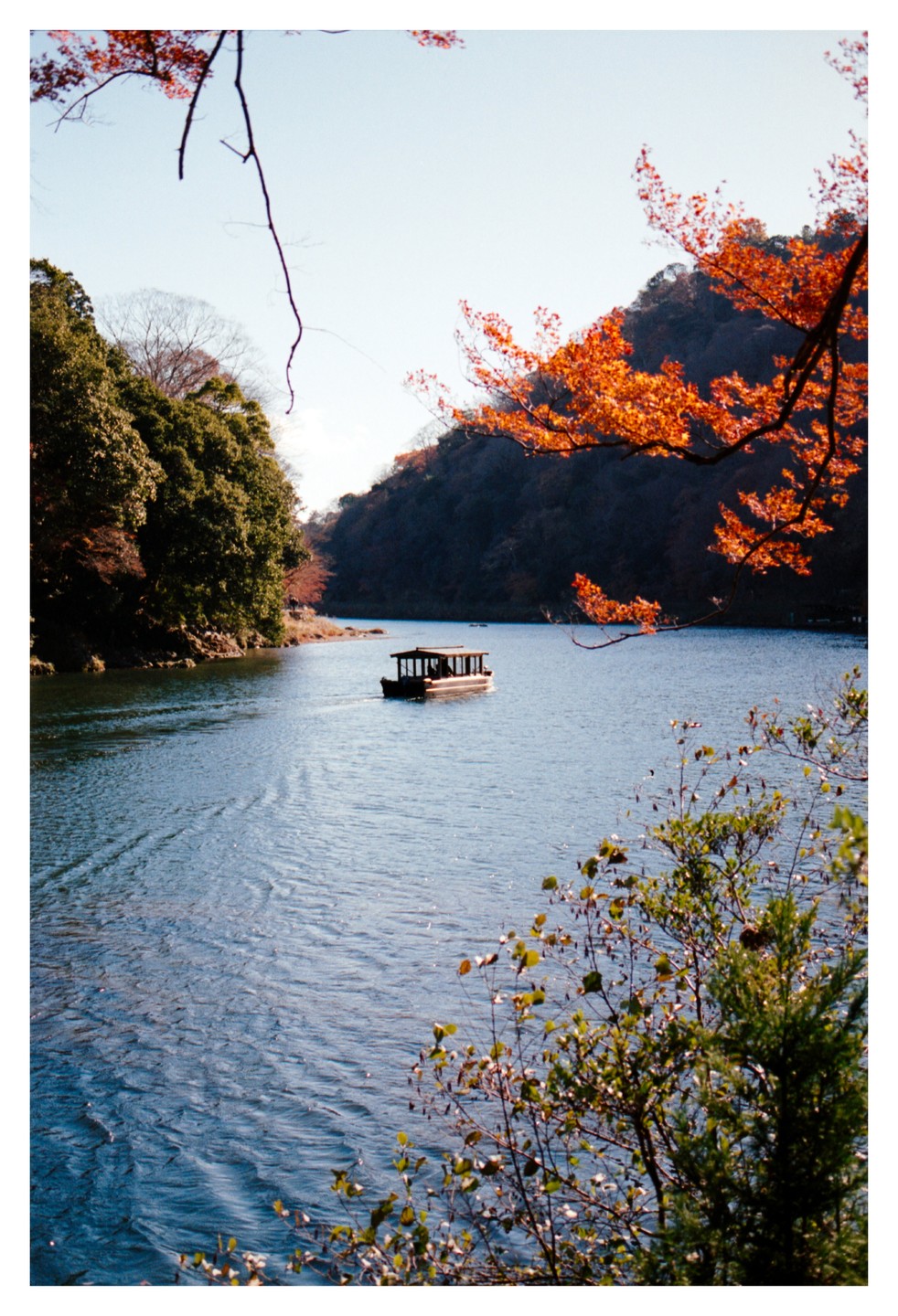 A small boat floats on a wide river surrounded by hills with autumn foliage.