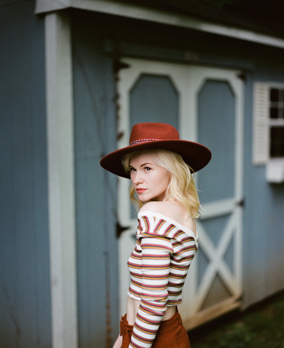 A woman wearing a hat and striped shirt looks over her shoulder at the viewer.