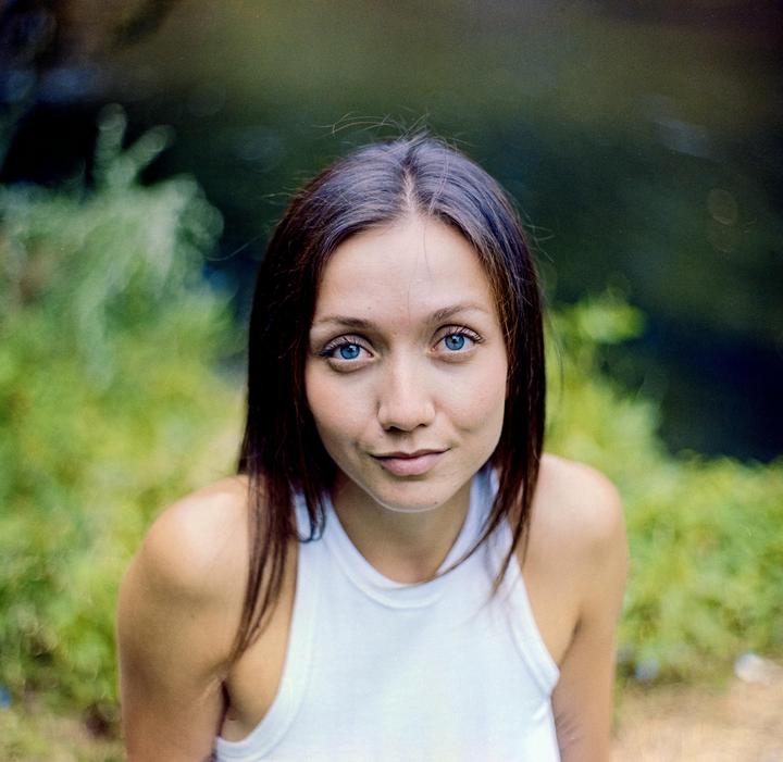 A woman with blue eyes looks directly at the viewer against a blurred green background.