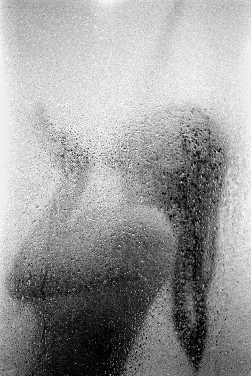 A person is visible behind a steamy glass surface covered in water droplets.