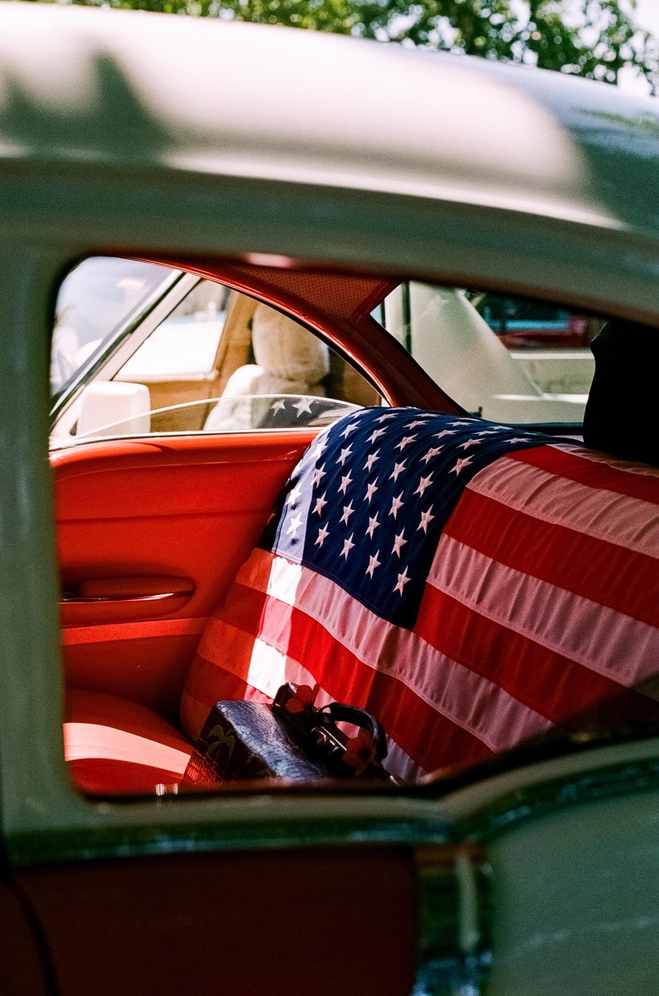 An American flag is draped over the back seat of a vintage car with red interior.