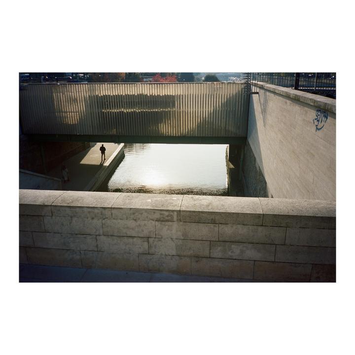 A man walks along a canal under a bridge in Paris.