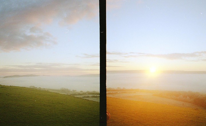 A split image shows a foggy landscape with a green hill on the left and a golden field with a bright sun on the right.
